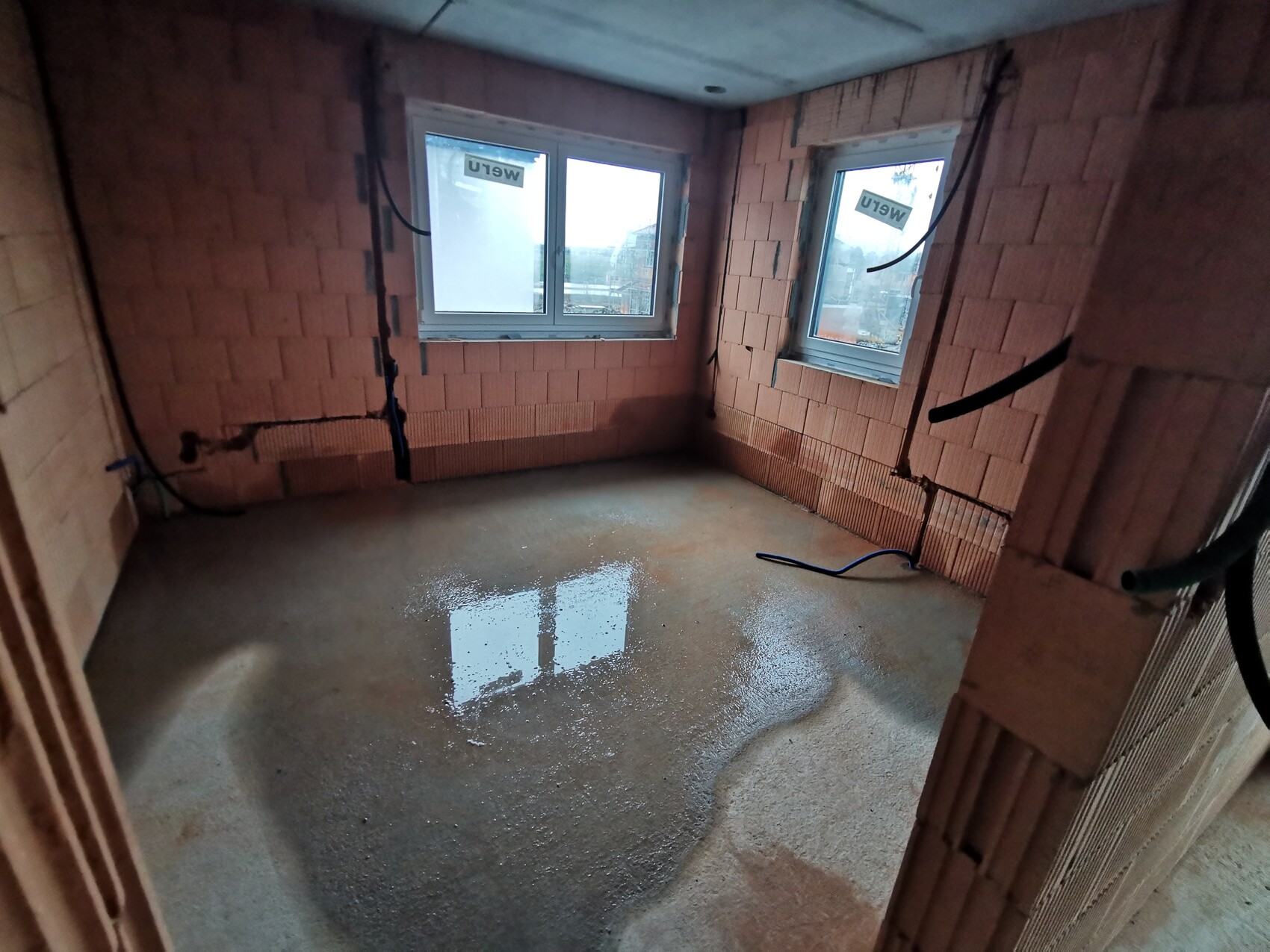 Unfinished interior made of bricks: two windows, wet floor and visible pipes