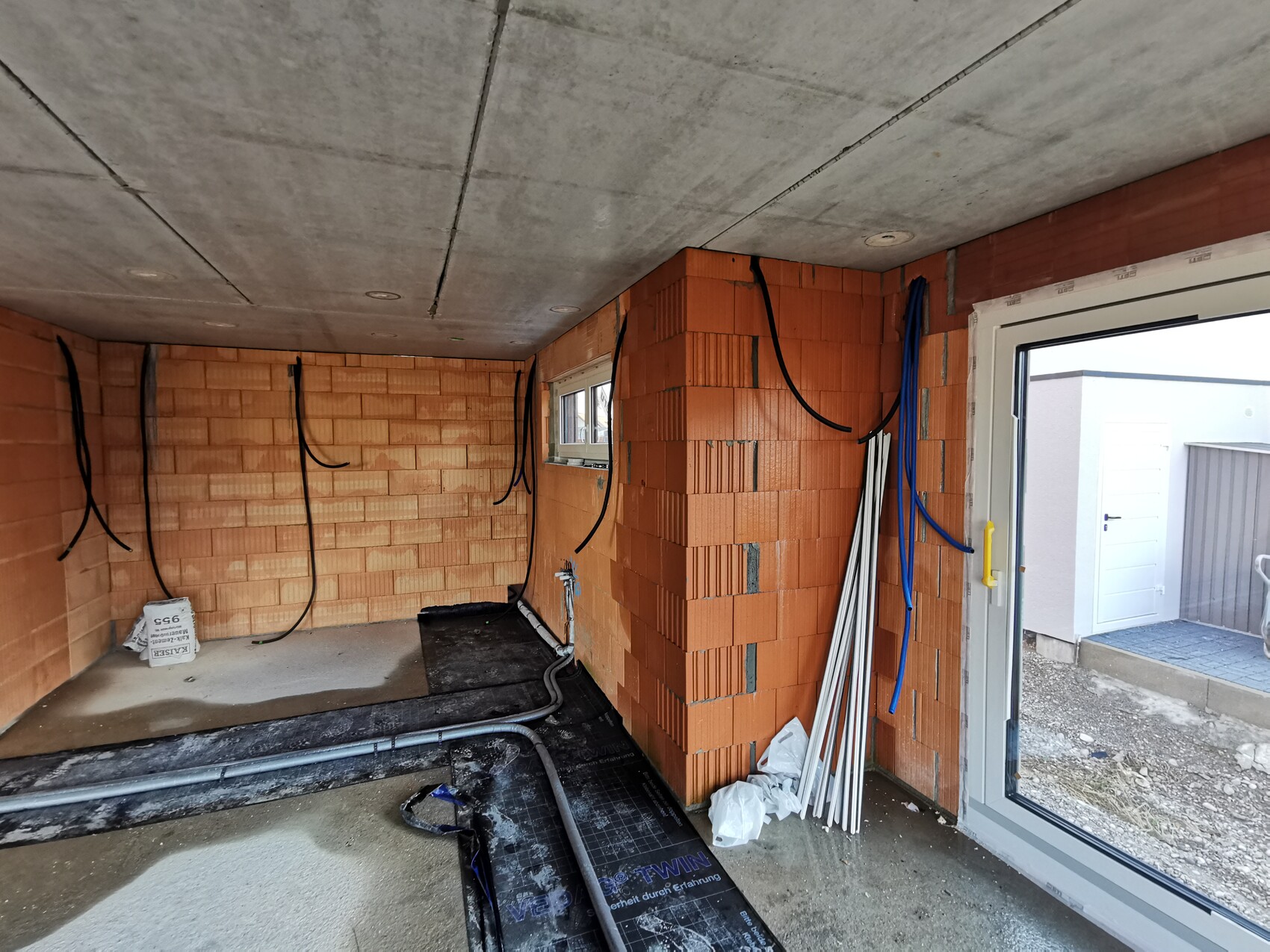 Unfinished interior with brick walls, hanging cables, pipes, window and glass door leading outside