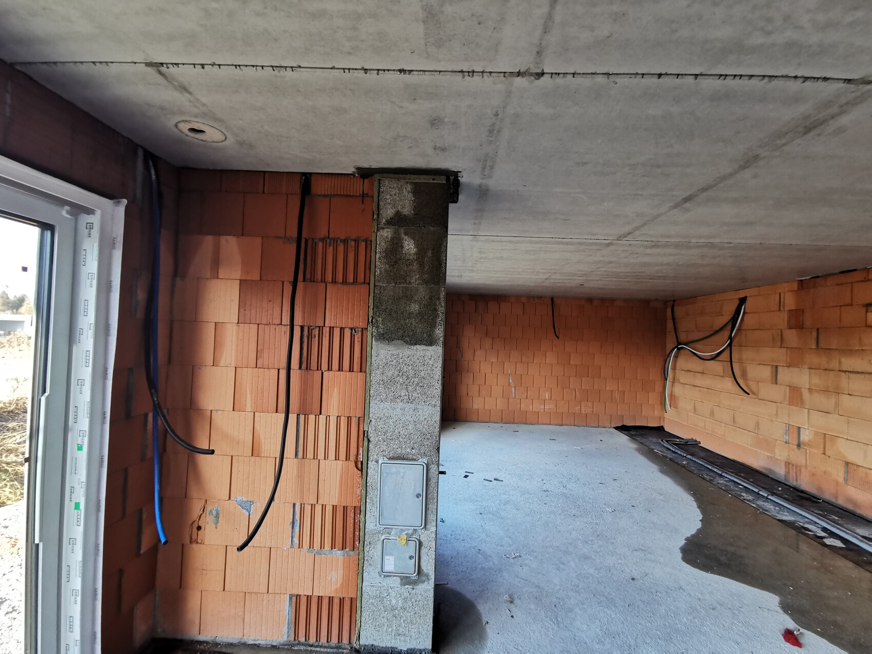 Unfinished interior with brick walls, concrete ceiling, loose cables and water puddle on the floor