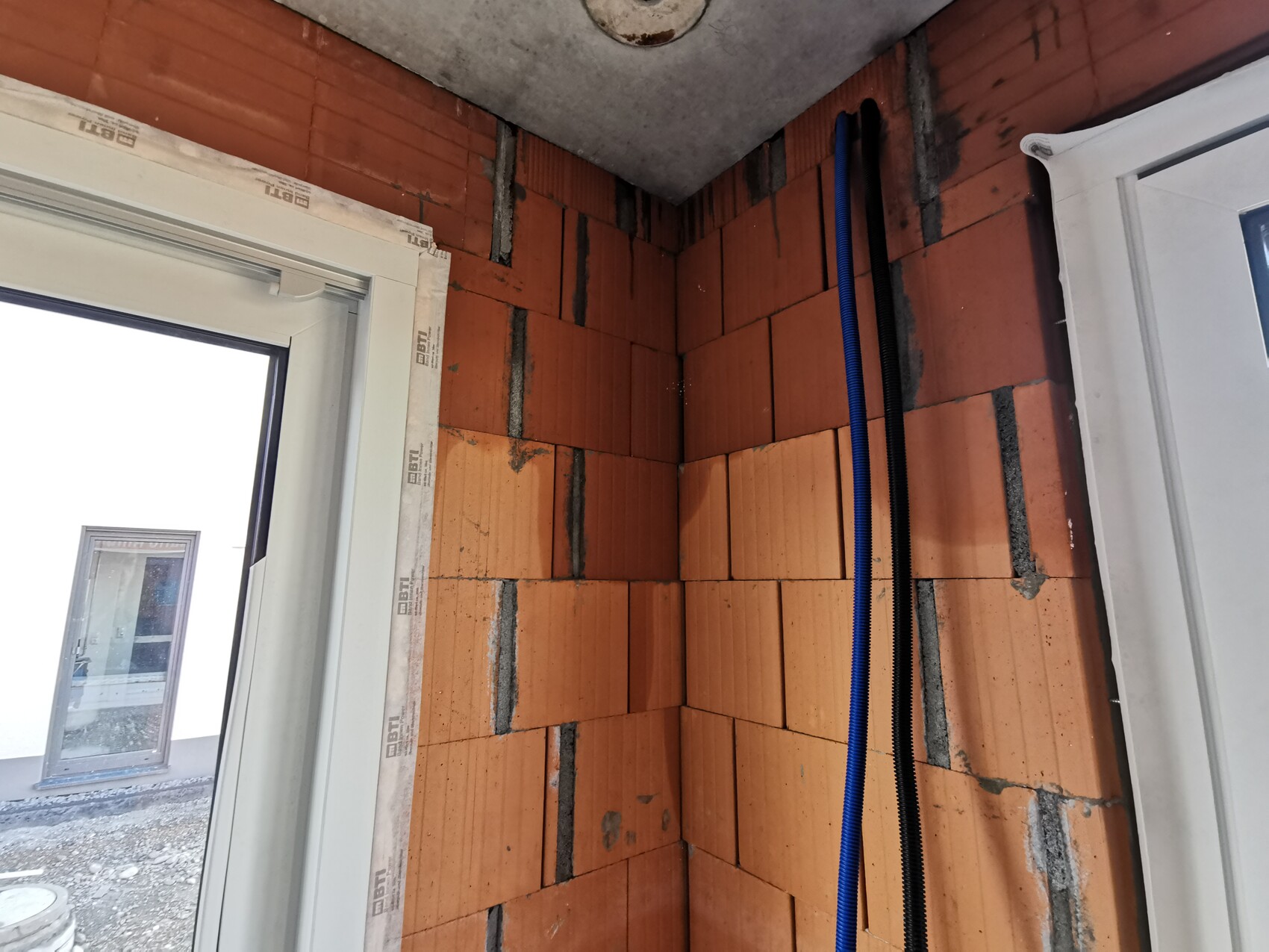 Shell structure room with exposed brick wall, blue and black cables, door frame on the left