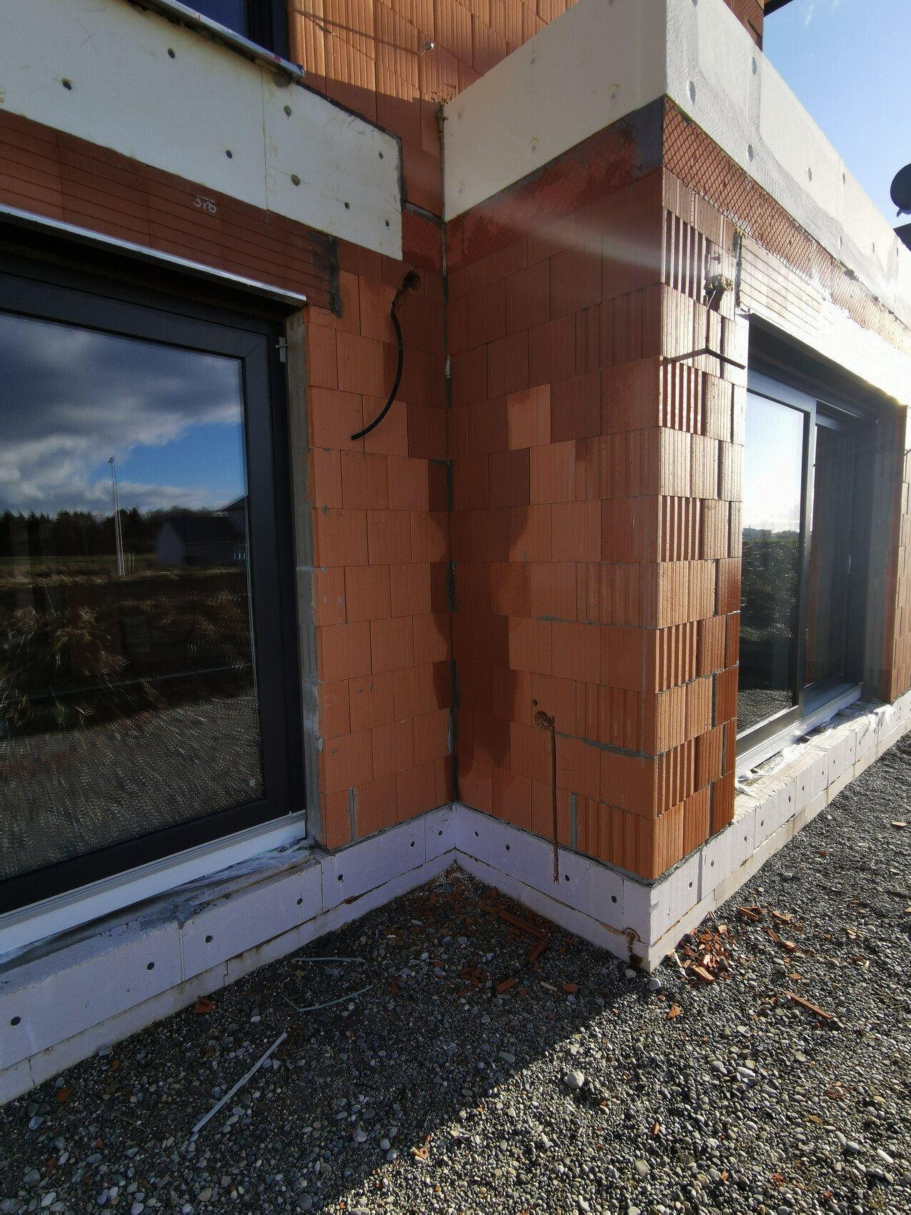 Shell structure made of red bricks on a building facade with two windows; gravel floor