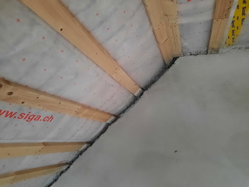 Substructure of a pitched roof: wooden beams, insulation membrane, white foil with red crosses.