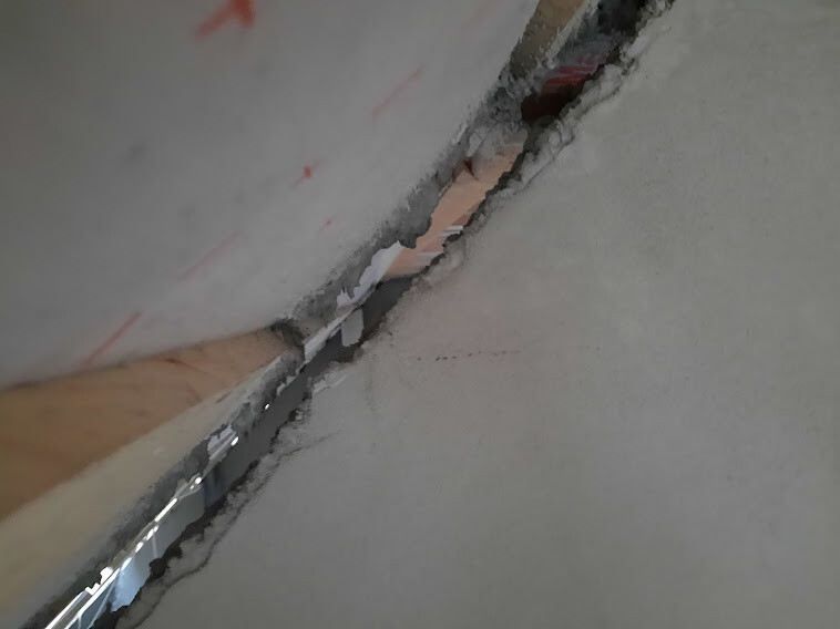 Slanted wall gap with broken-off plaster layer and visible inner material.