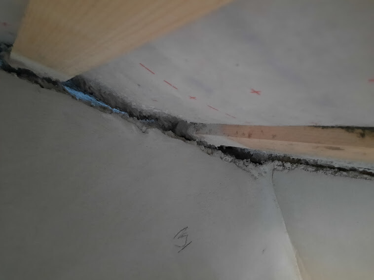 Close-up of a gap in drywall with joint compound, wooden strip on the edge, red markings.