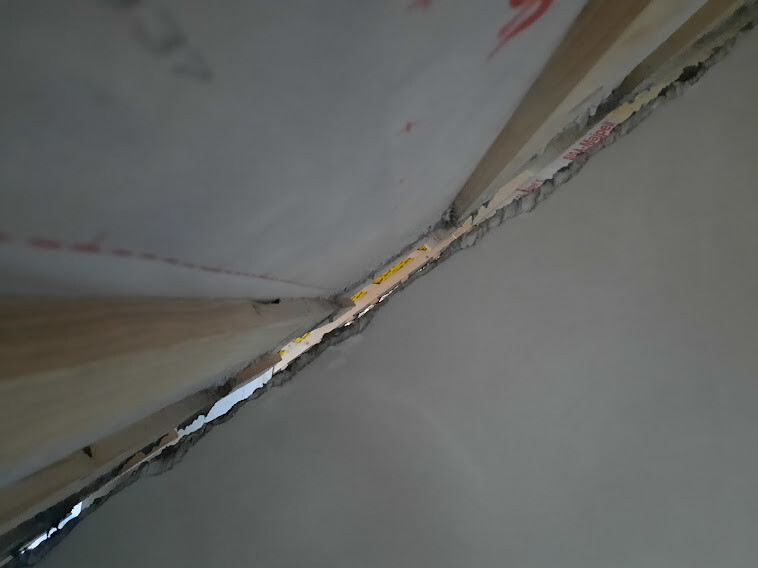 Close-up of a wall-ceiling connection with wooden laths, plaster crack, and insulation material.