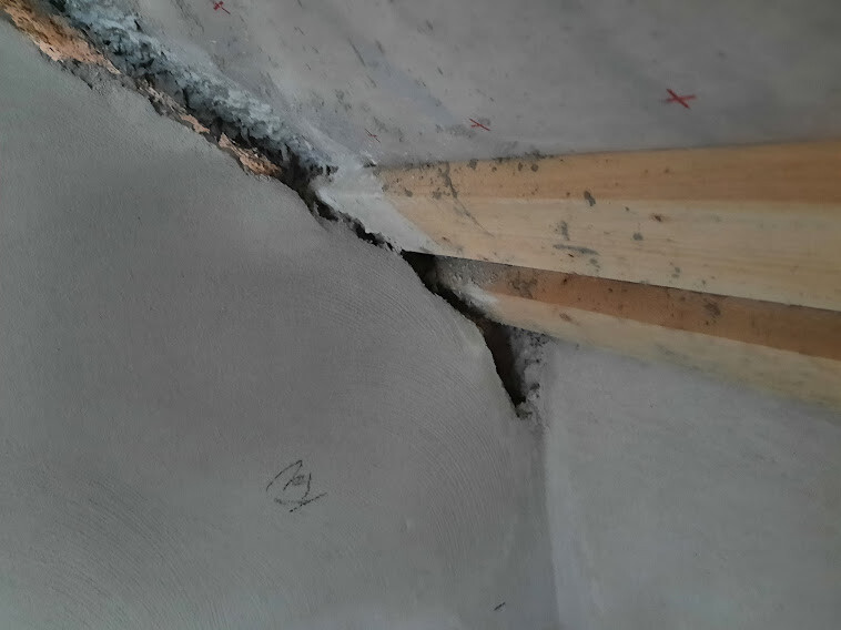 Inner corner of a wall-ceiling connection with crack and visible wooden laths.