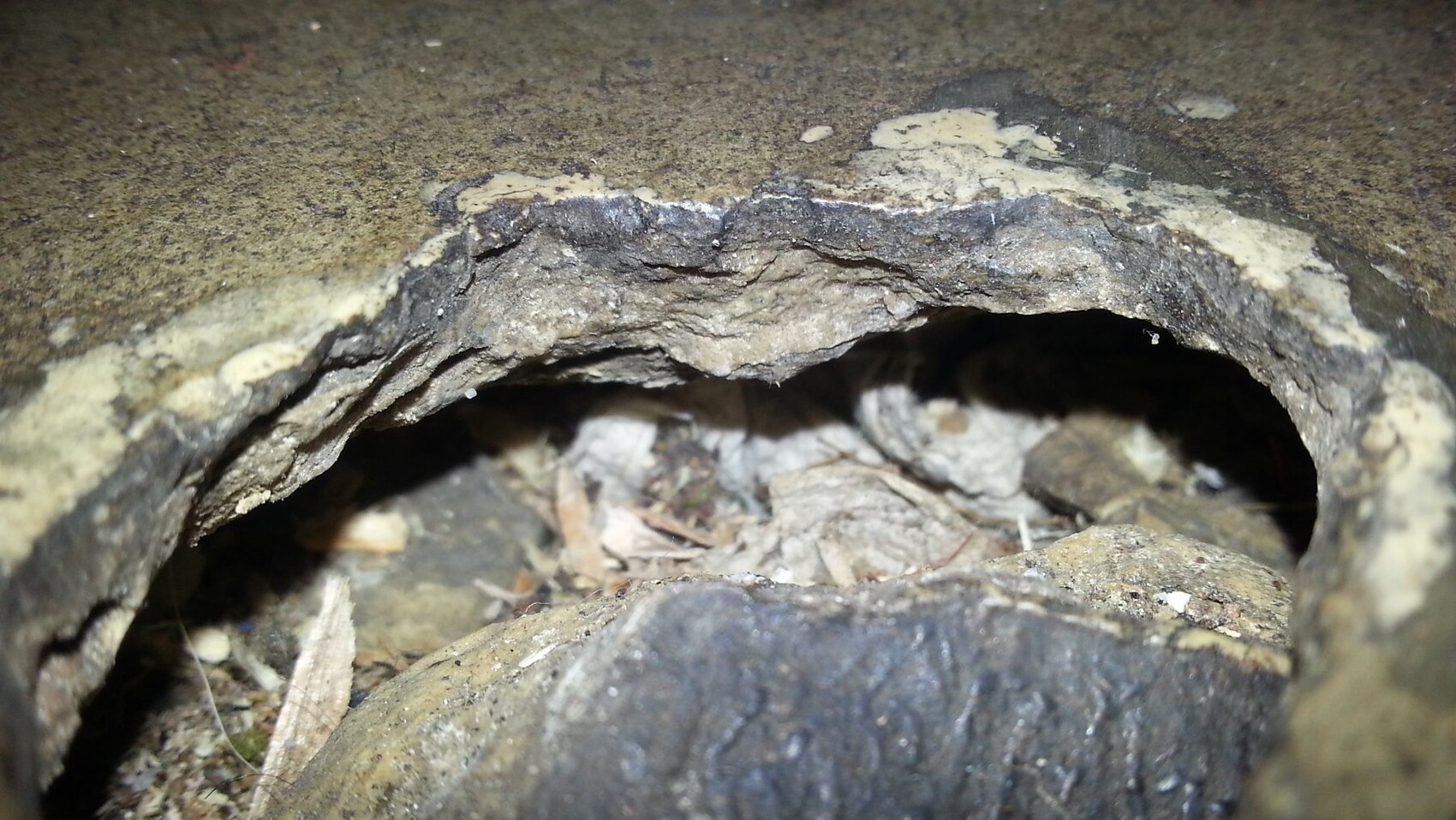 Close-up of a hole in a concrete surface with crumbs and dust