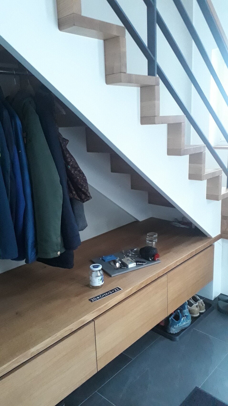 Hallway under the stairs: jackets hanging on the left, wooden bench with items, shoes underneath.