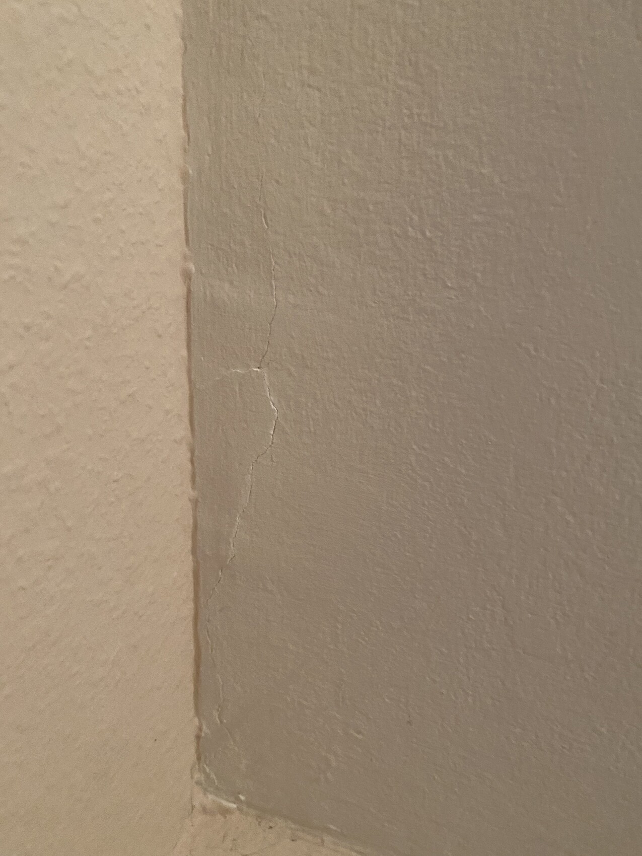 Close-up of an interior wall corner with a fine crack in the plaster along the edge.