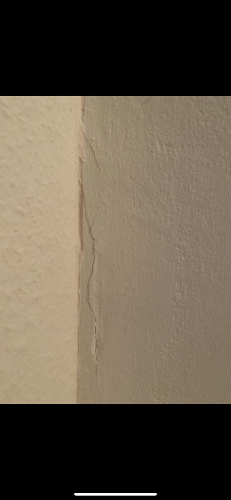 Fine vertical crack in plaster on a wall near the corner, beige surface.