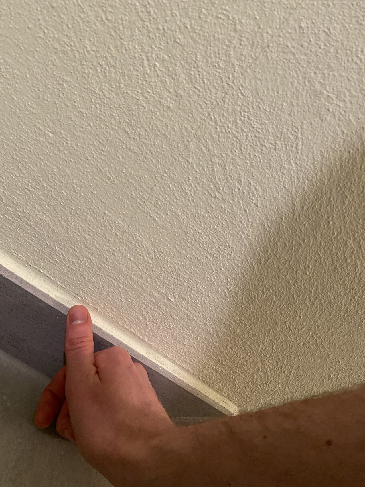 Close-up of a hand touching the edge between a gray area and rough beige wall.