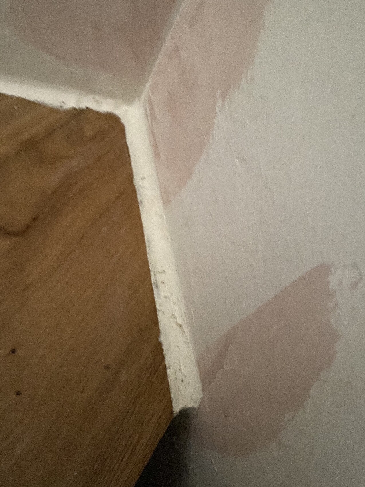 Corner of a room: pink plastered wall, wooden floor, white baseboard.