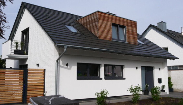 Modern white single-family house with dark pitched roof, wooden dormer, and garden.