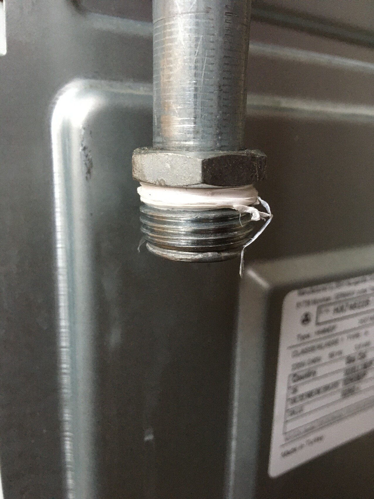 Close-up of a metal pipe with threading, white Teflon tape wrapped around the connection.