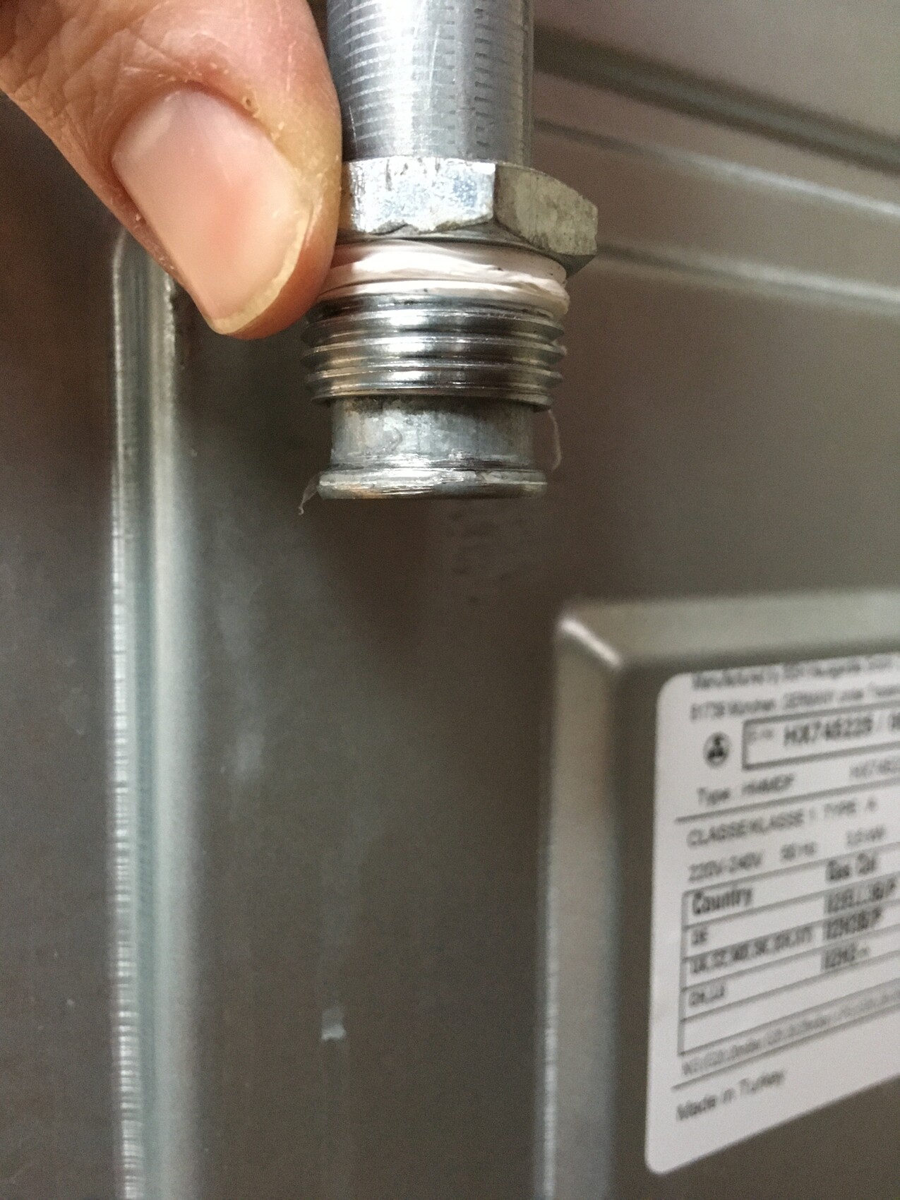 Hand on a screwed metal threaded connection, sealing paste visible on the thread.