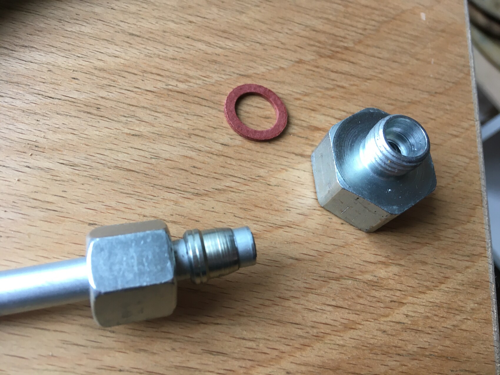 Two metal threaded fittings and a red sealing ring lie on a wooden table.
