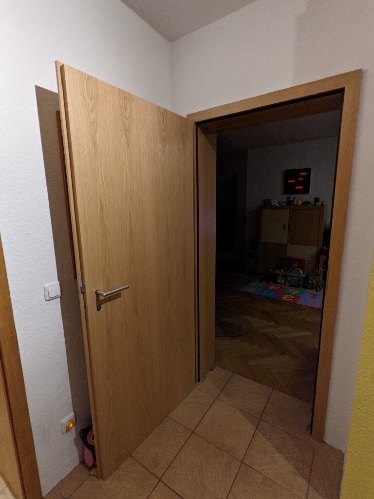 Open wooden door in hallway leads to living area with play area in the background.