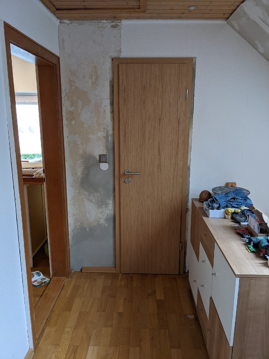 Hallway with wooden door, plastered wall and sideboard with tools.