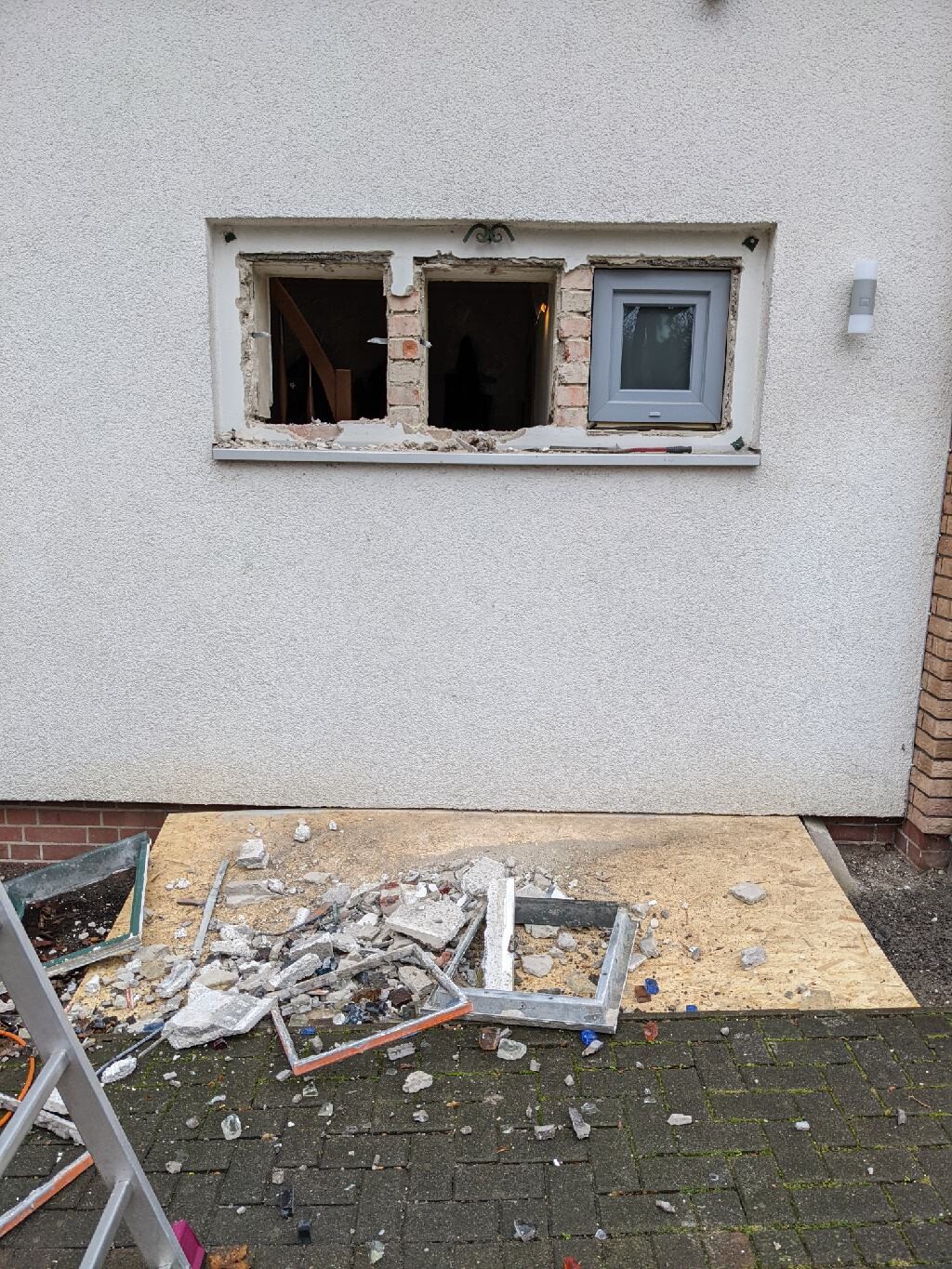 Damaged exterior wall with open window niche, construction debris and fragments in front.