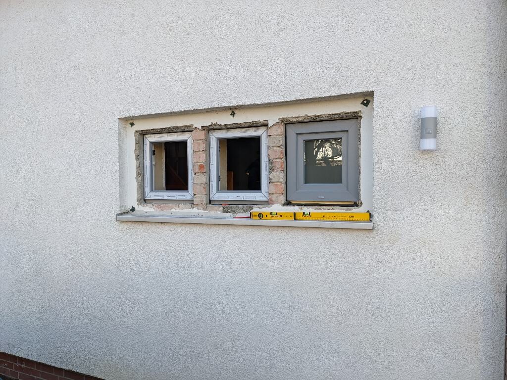 Exterior wall with three windows; damaged areas around the frame; level lies on the windowsill.