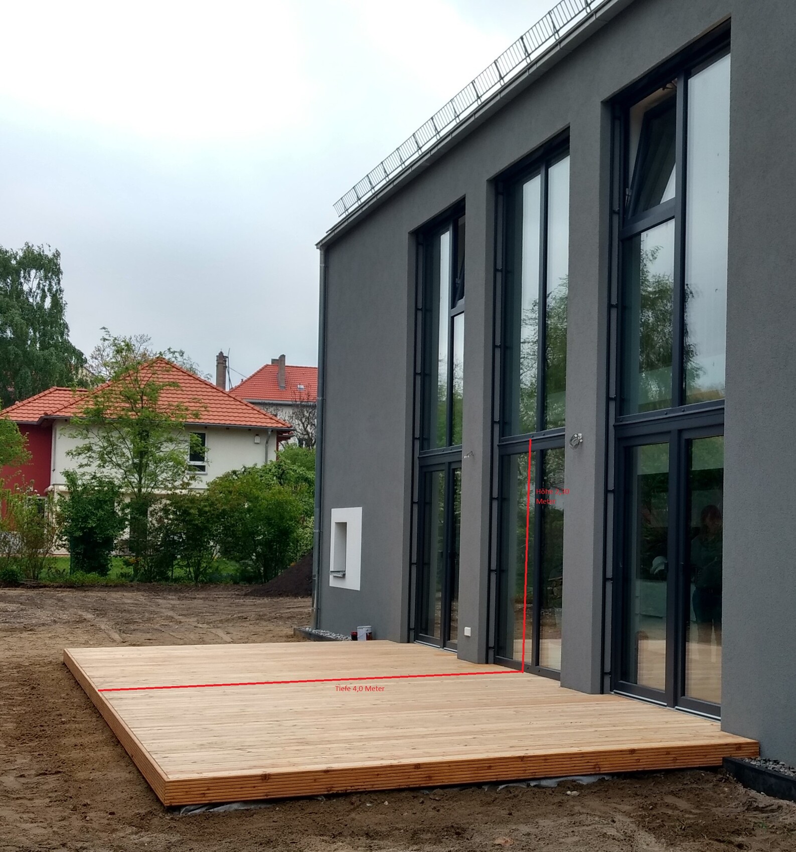 Modern gray facade with large glass windows and wooden terrace outdoors.