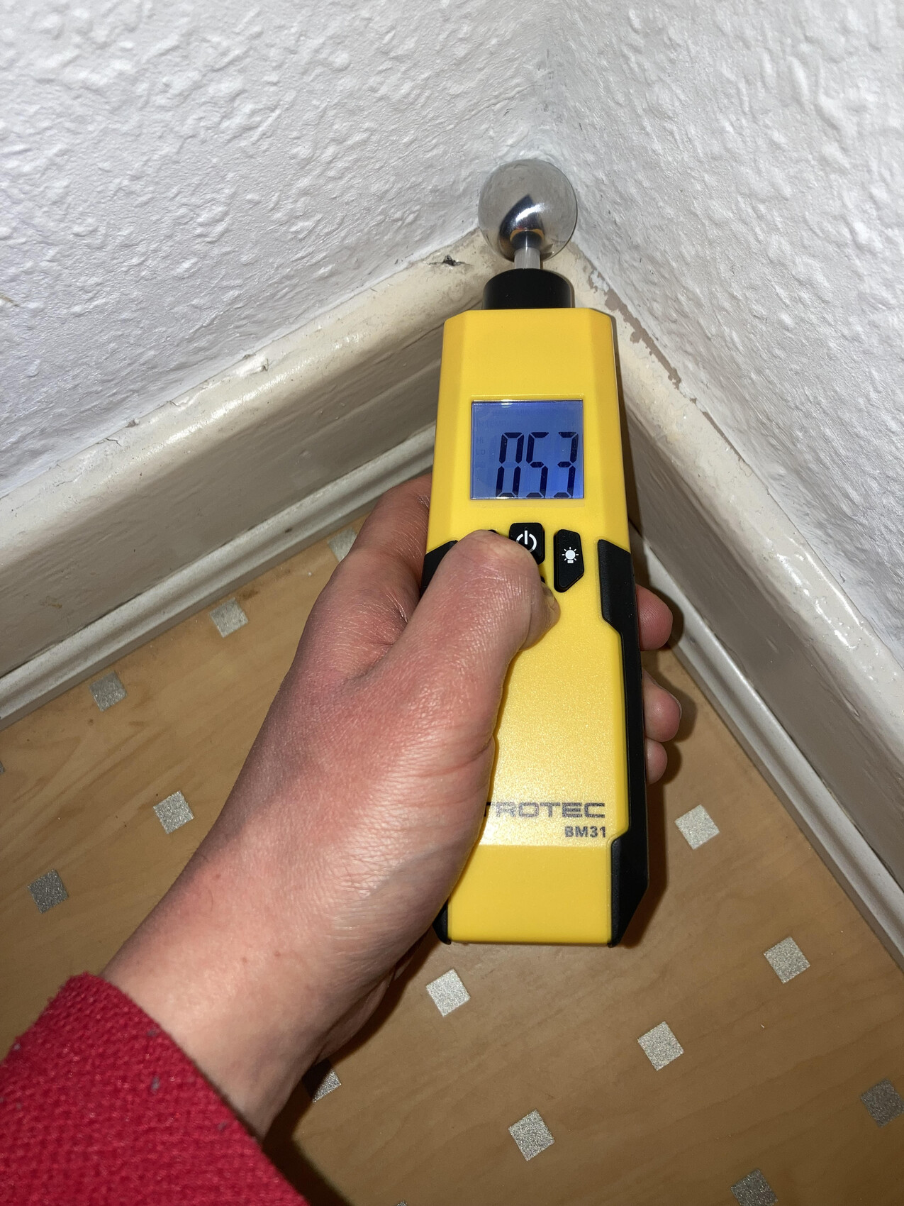 Hand holding yellow Trotec BM31 device at wall corner; display shows 0.53.