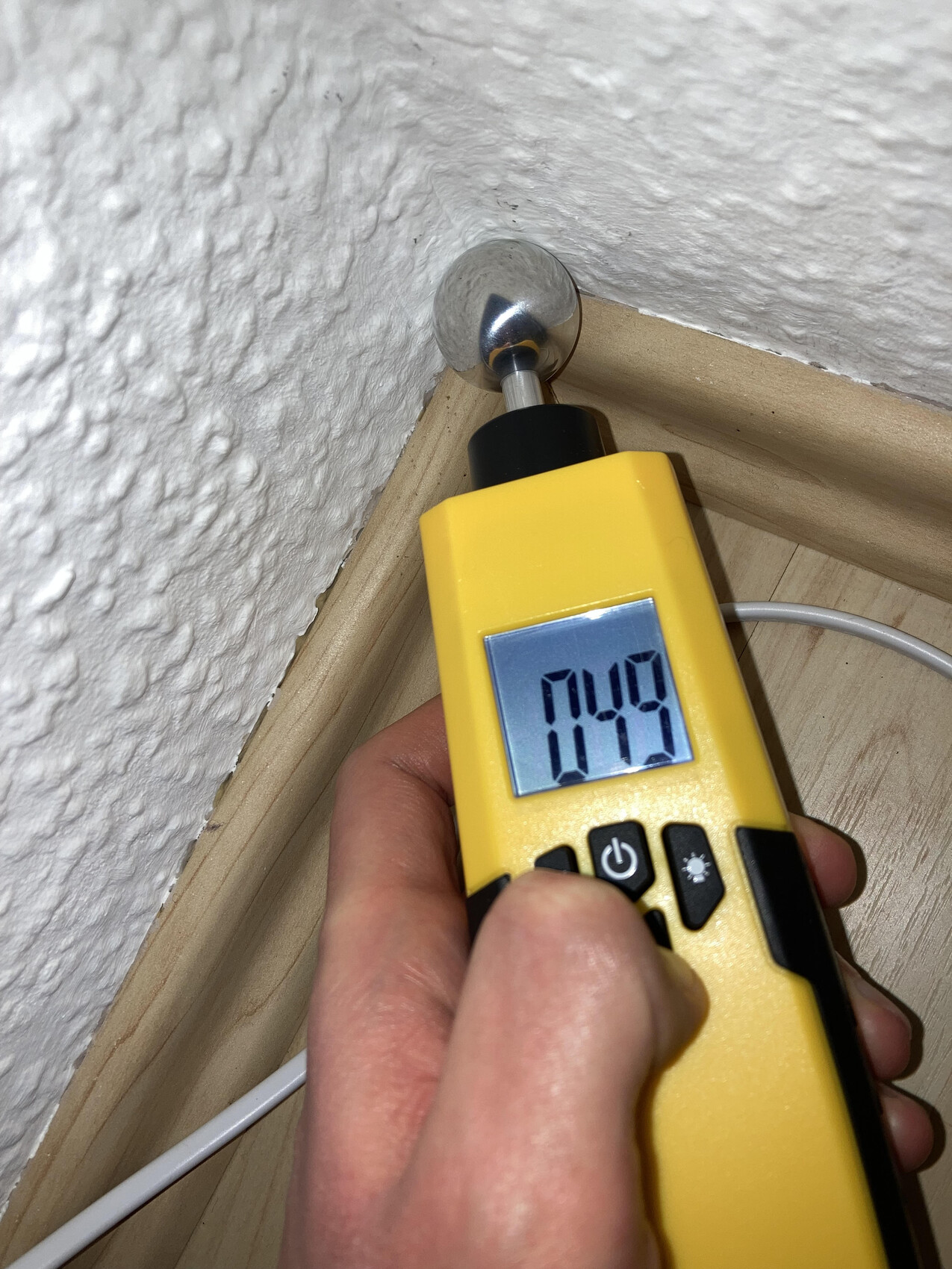 Yellow meter with display held against round metal cap in wall; reading 0.49.