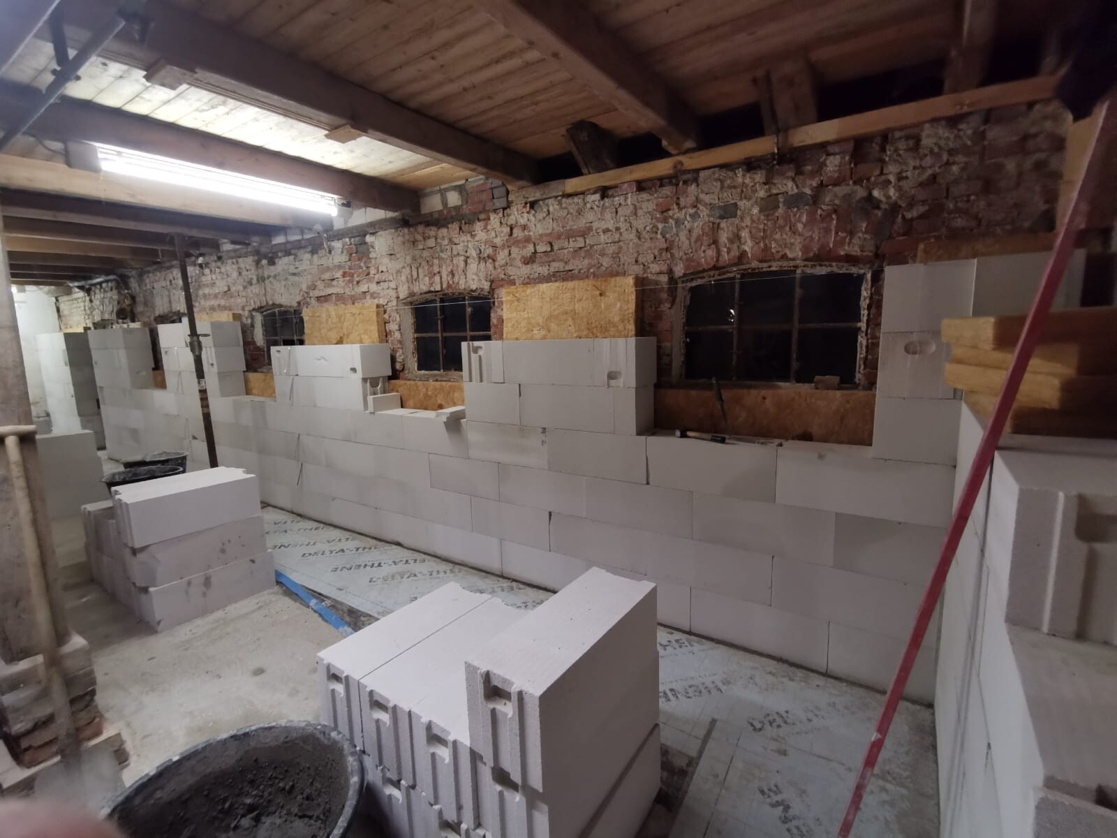 Basement: new interior wall made of aerated concrete blocks under construction; brick wall and wooden beam ceiling visible behind.