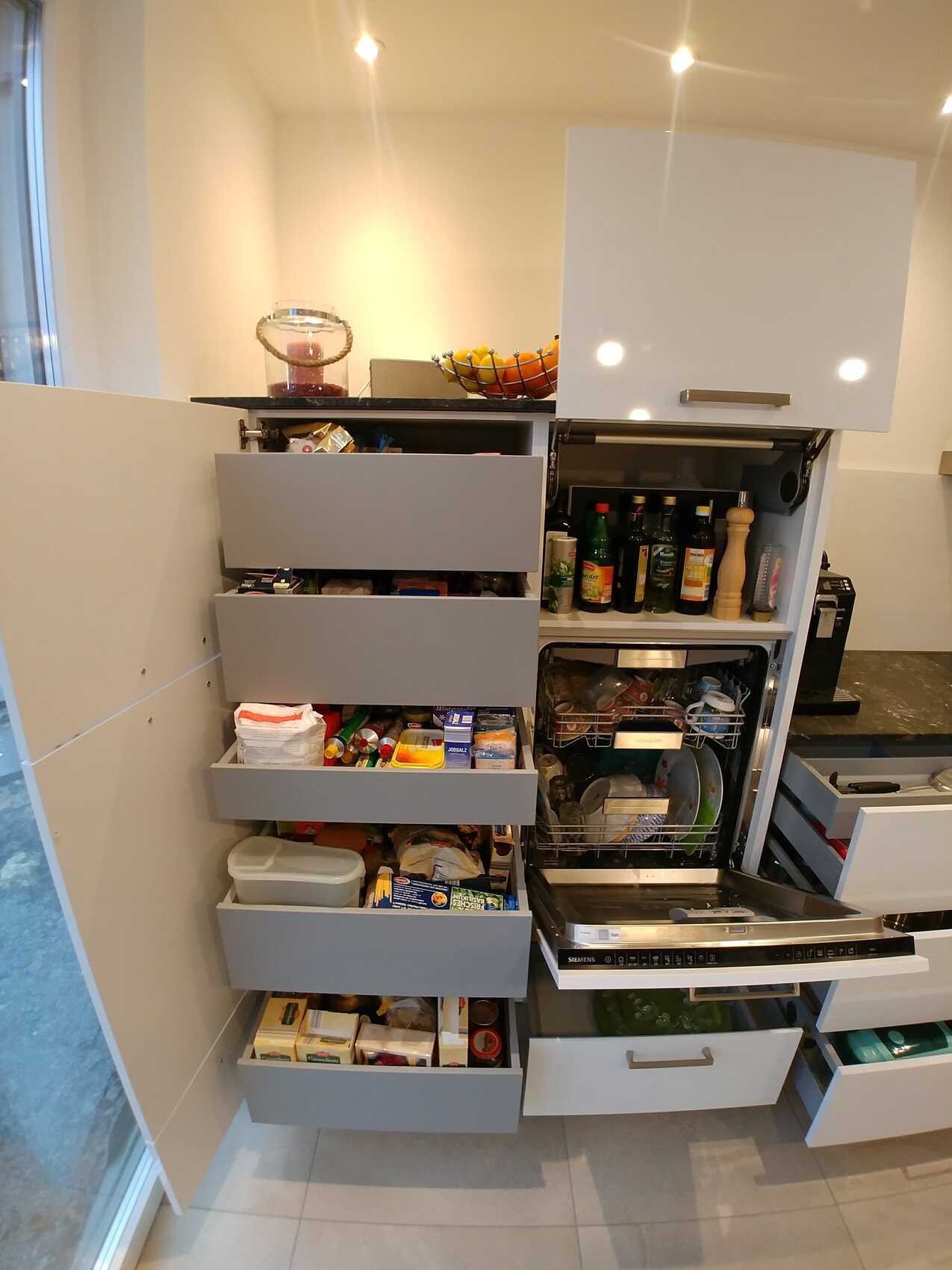 Modern kitchen with open drawers, dishwasher open, fruit basket on the countertop.