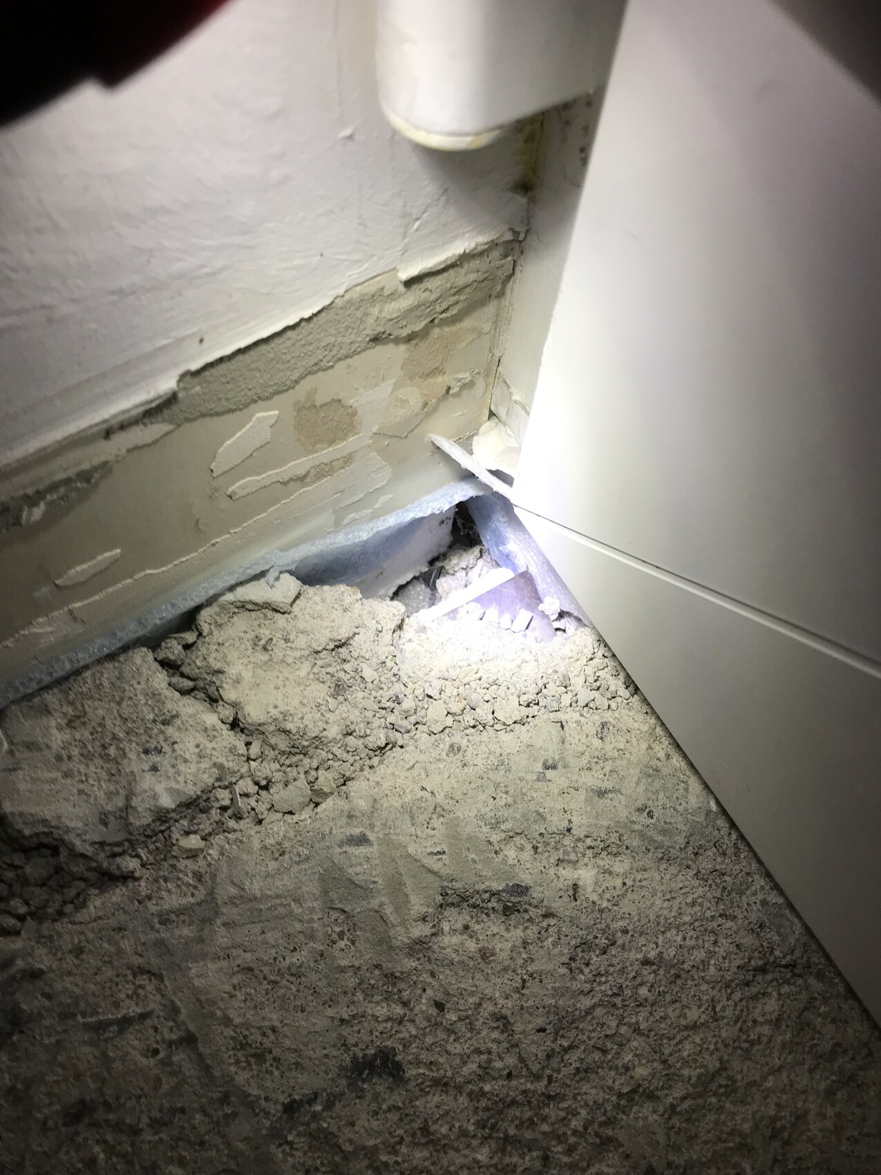 Wall with peeling plaster, pipe in corner; dust and debris on the floor.