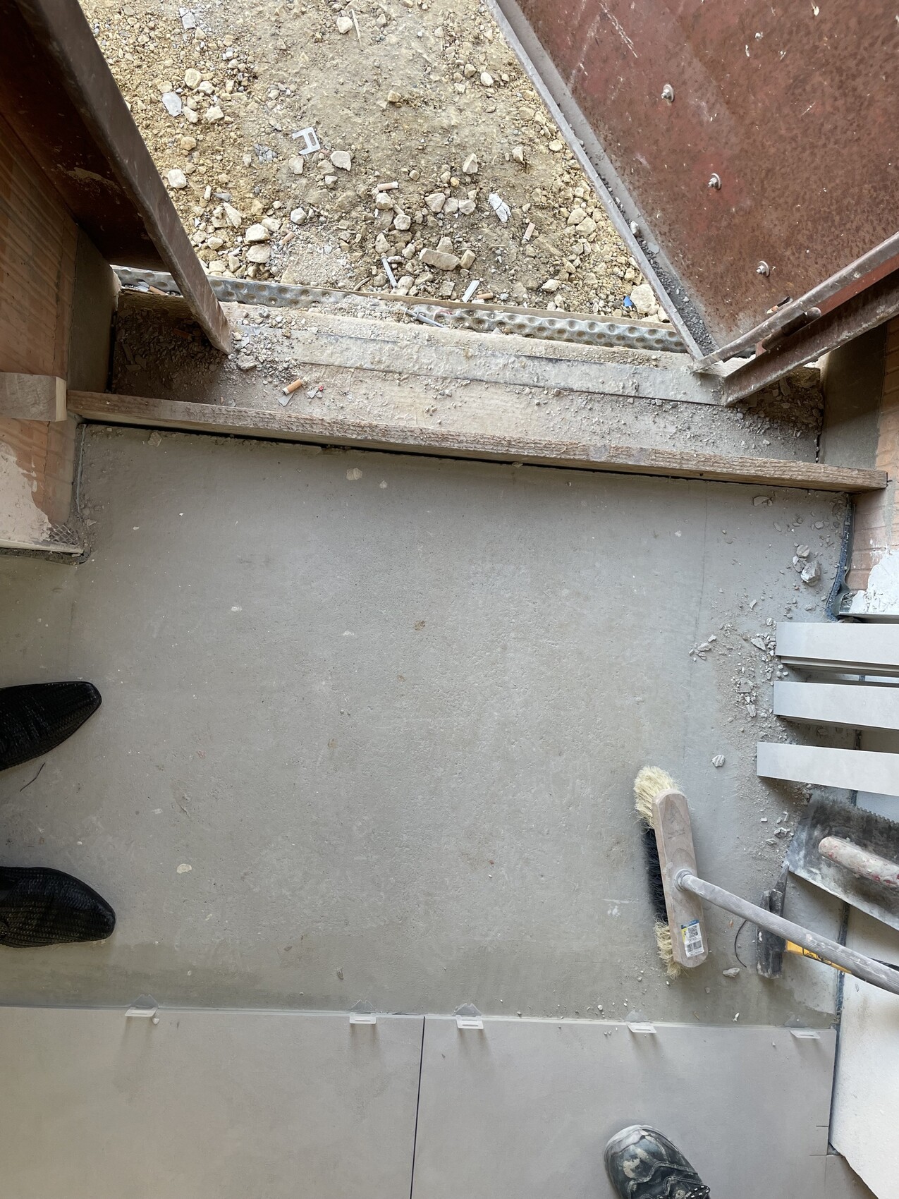 Construction site indoors: concrete floor, cleaning broom, and building materials.