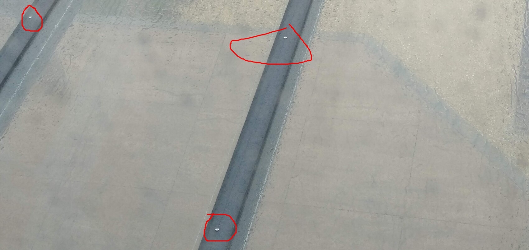 Top view of gray concrete floor with dark joint; three silver screws.