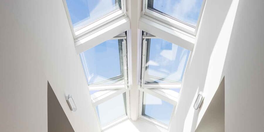 Roof window in white ceiling with glass panes and view of blue sky.