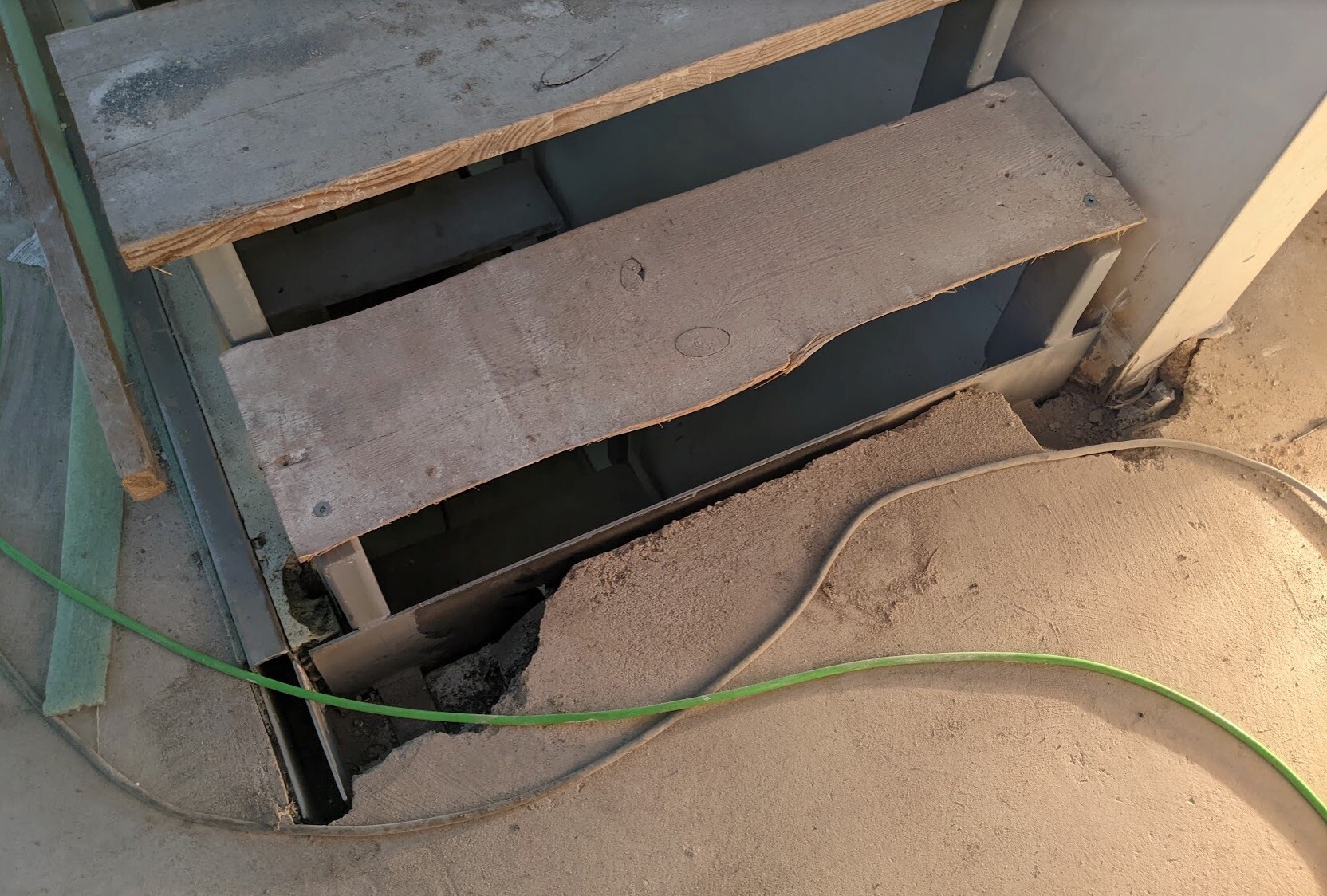Wooden steps of a temporary construction staircase, dust, open gap, green cable on the floor.