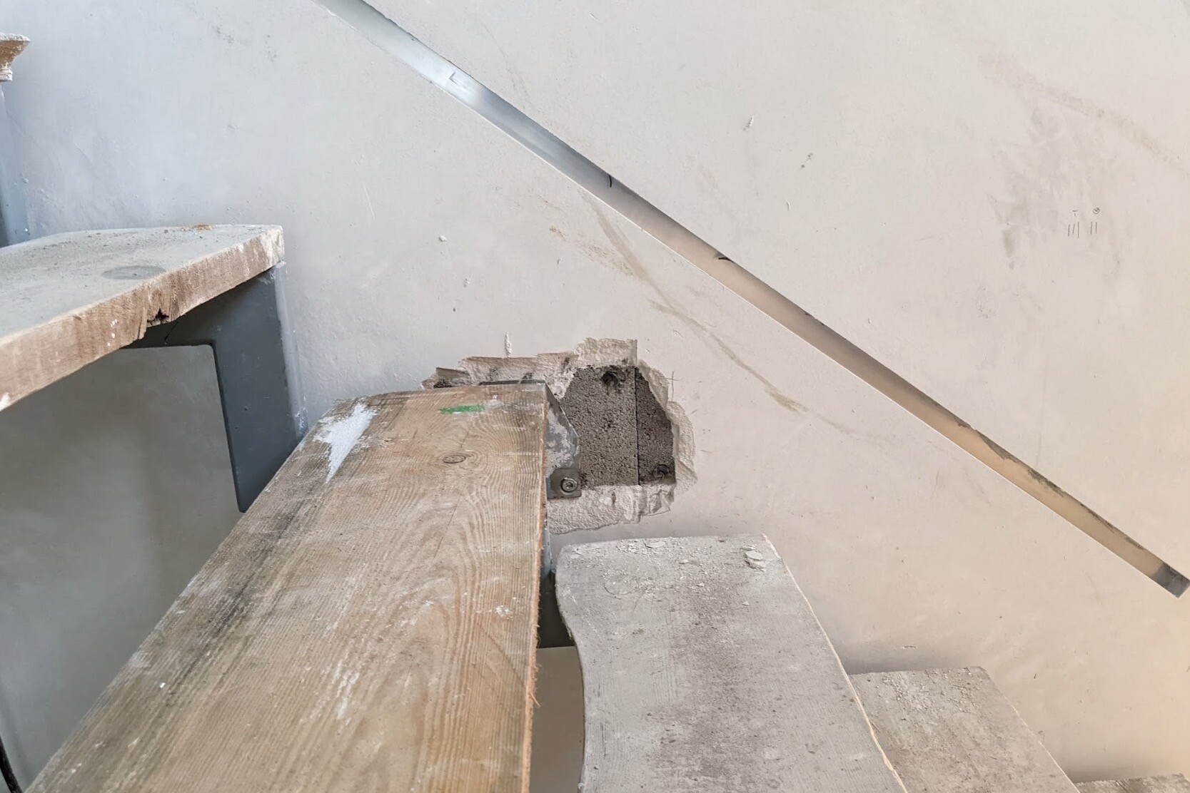 Wooden staircase on site; hole in concrete wall with metal bar beside it.