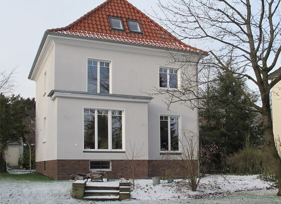 Weißes zweistöckiges Haus mit rotem Ziegeldach, großen Fenstern und leichter Schneedecke.