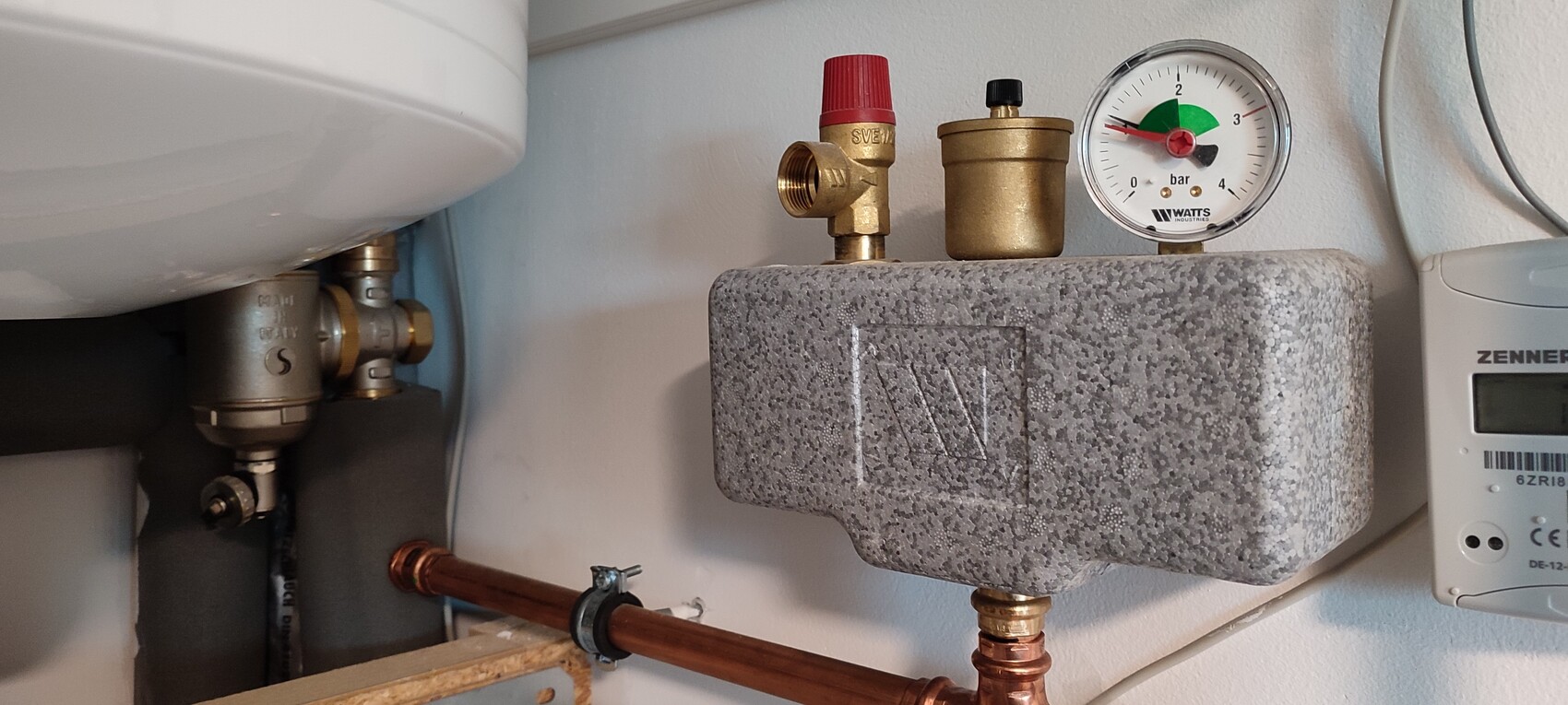 Heating system: pressure gauge (bar) with red valve, gray insulation box, and copper pipes.