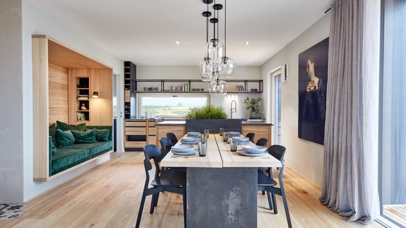 Modern kitchen and dining area with long table, black chairs, pendant lamps and bench seating.