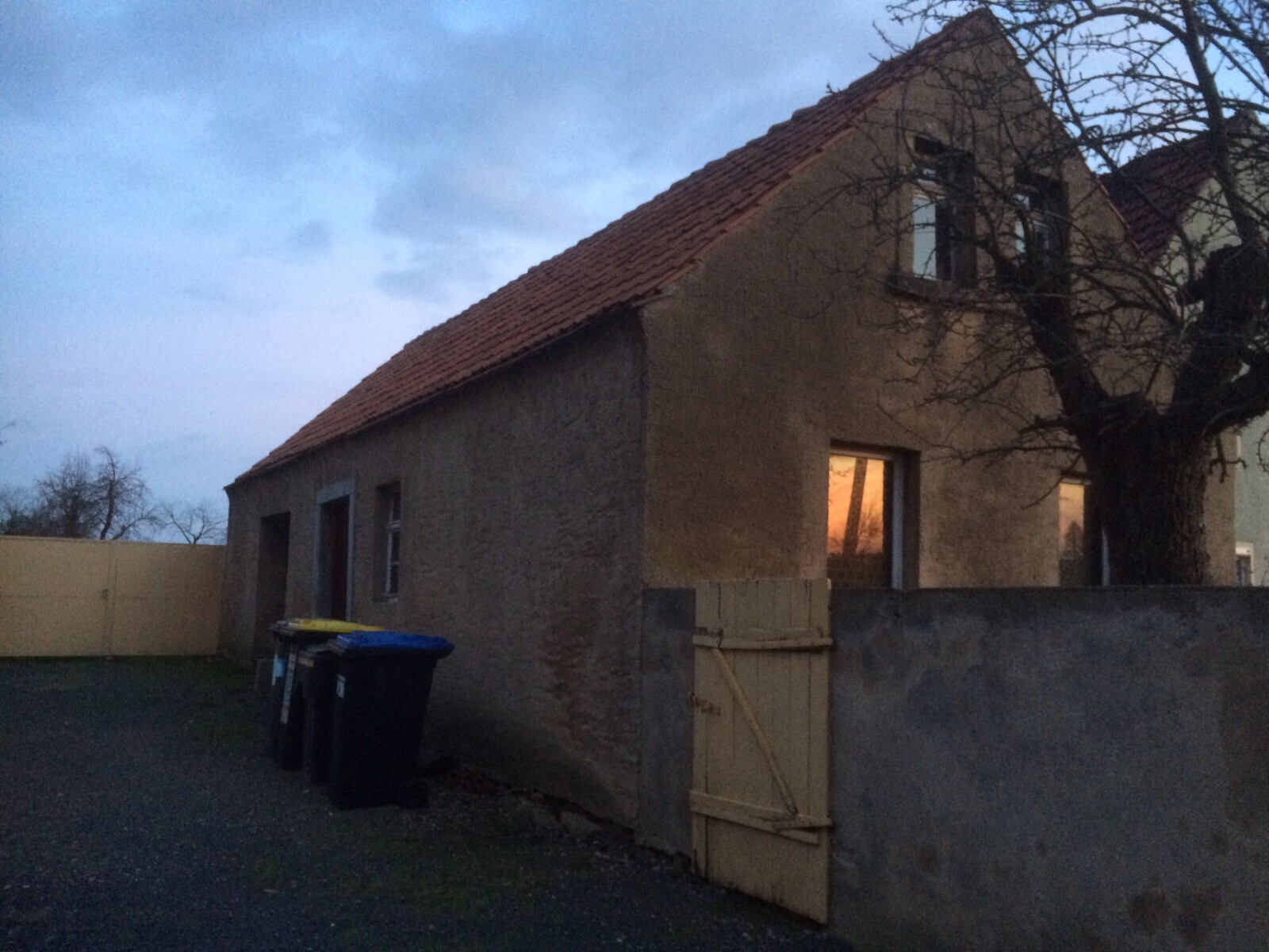Exterior view of an old house with red tiled roof, tree and fence