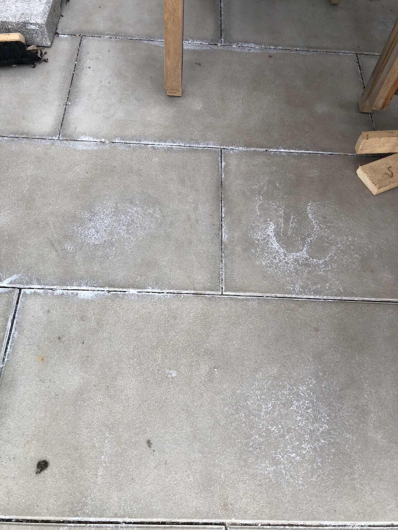 Exterior concrete slabs with white dust marks between the joints; wooden parts of a table frame.