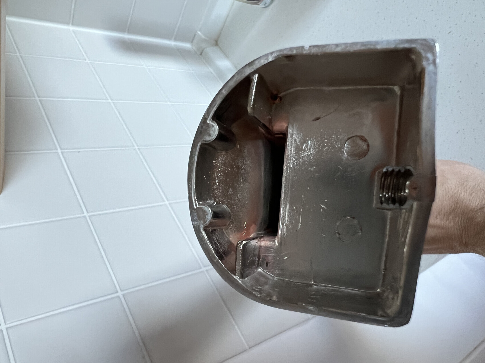 Close-up of a metallic plumbing part with thread in front of tiles.