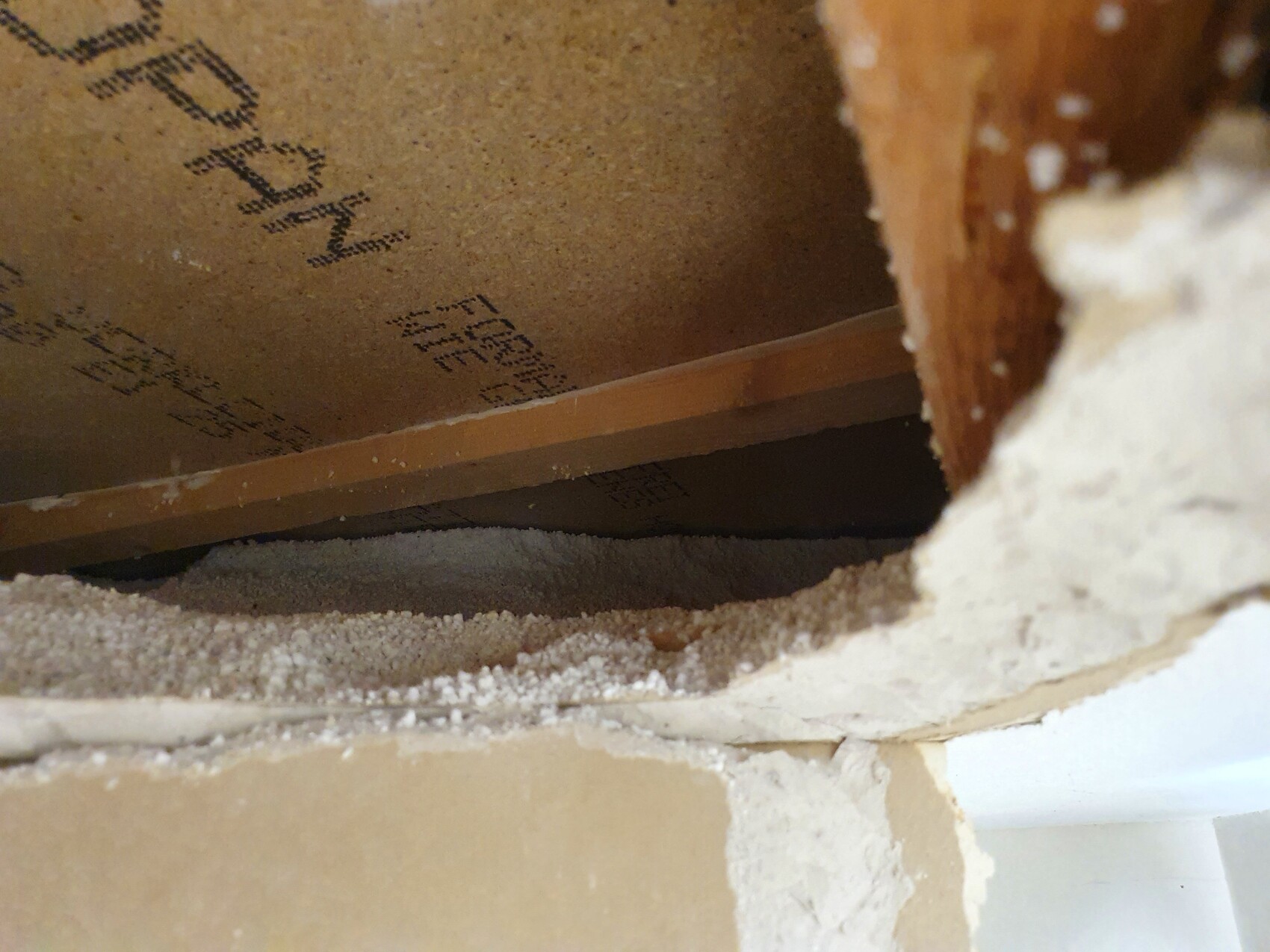 Open wall opening with wooden frame, dust and plaster residues in the room.