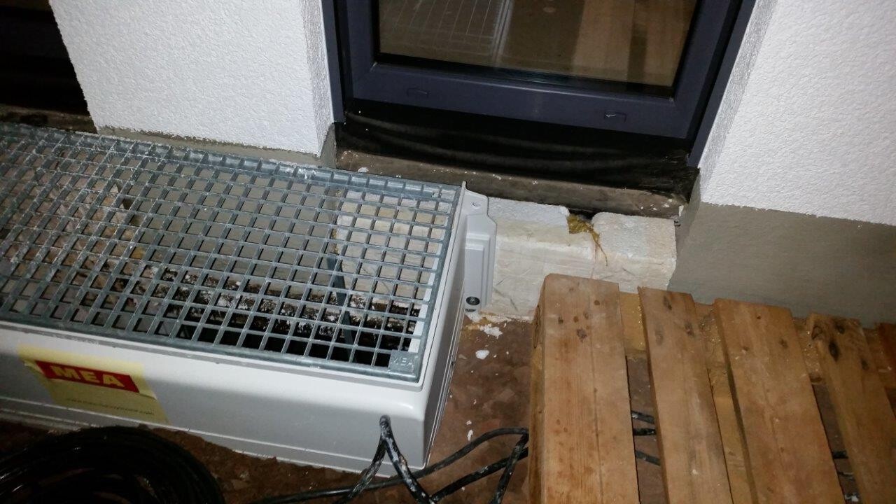 Metal device with grid mesh standing next to a door; wooden boards and cables lying on the floor.