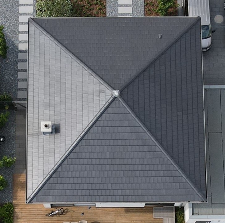 Bird’s-eye view: roof with light gray and dark gray areas, X-shape in the center; wooden terrace in front.