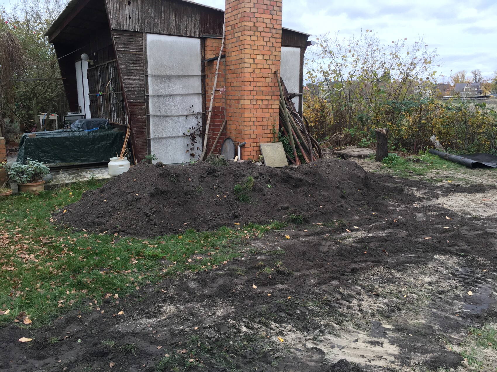 Earthen mound in front of the house with brick chimney; shovels standing nearby.