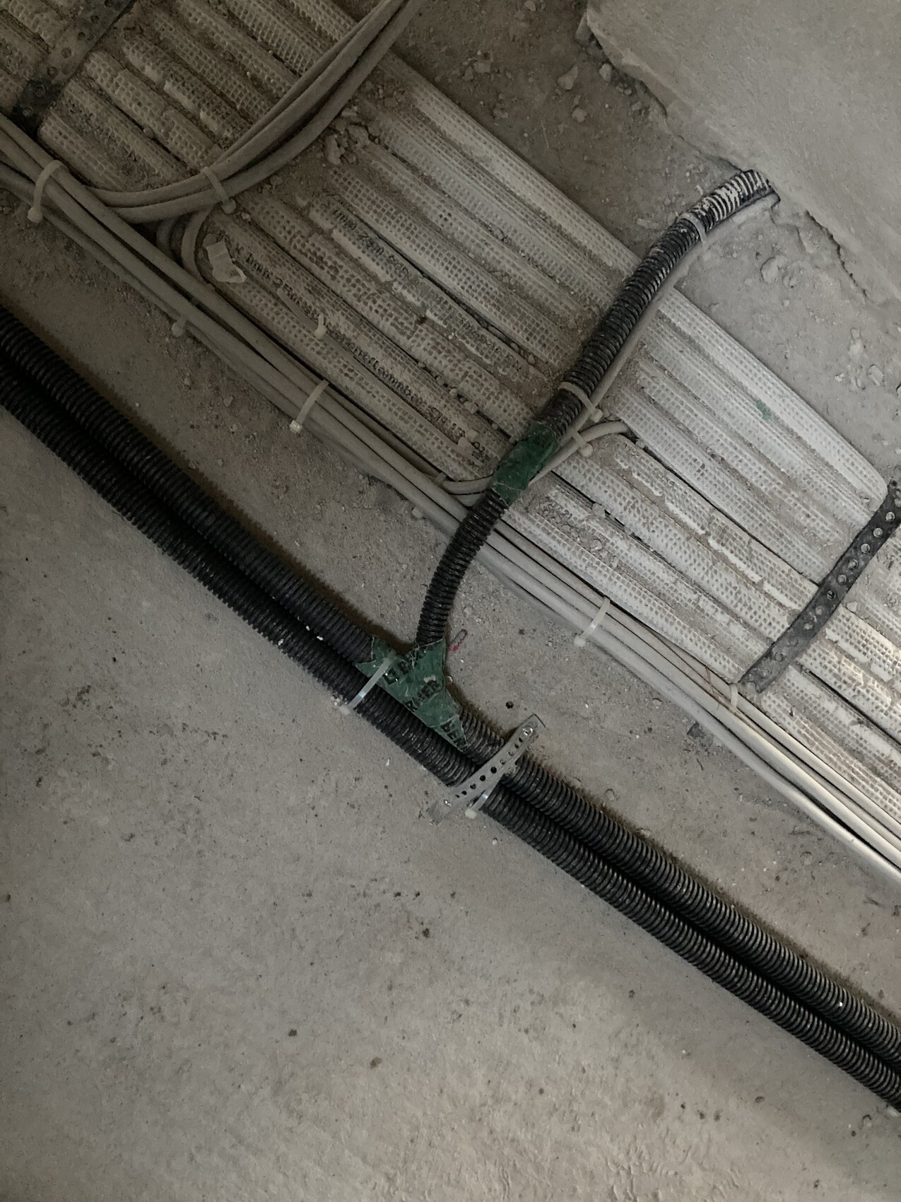 Kabelinstallation auf Baustelle: schwarze Kabelrohre und graue Leitungen auf staubigem Boden.