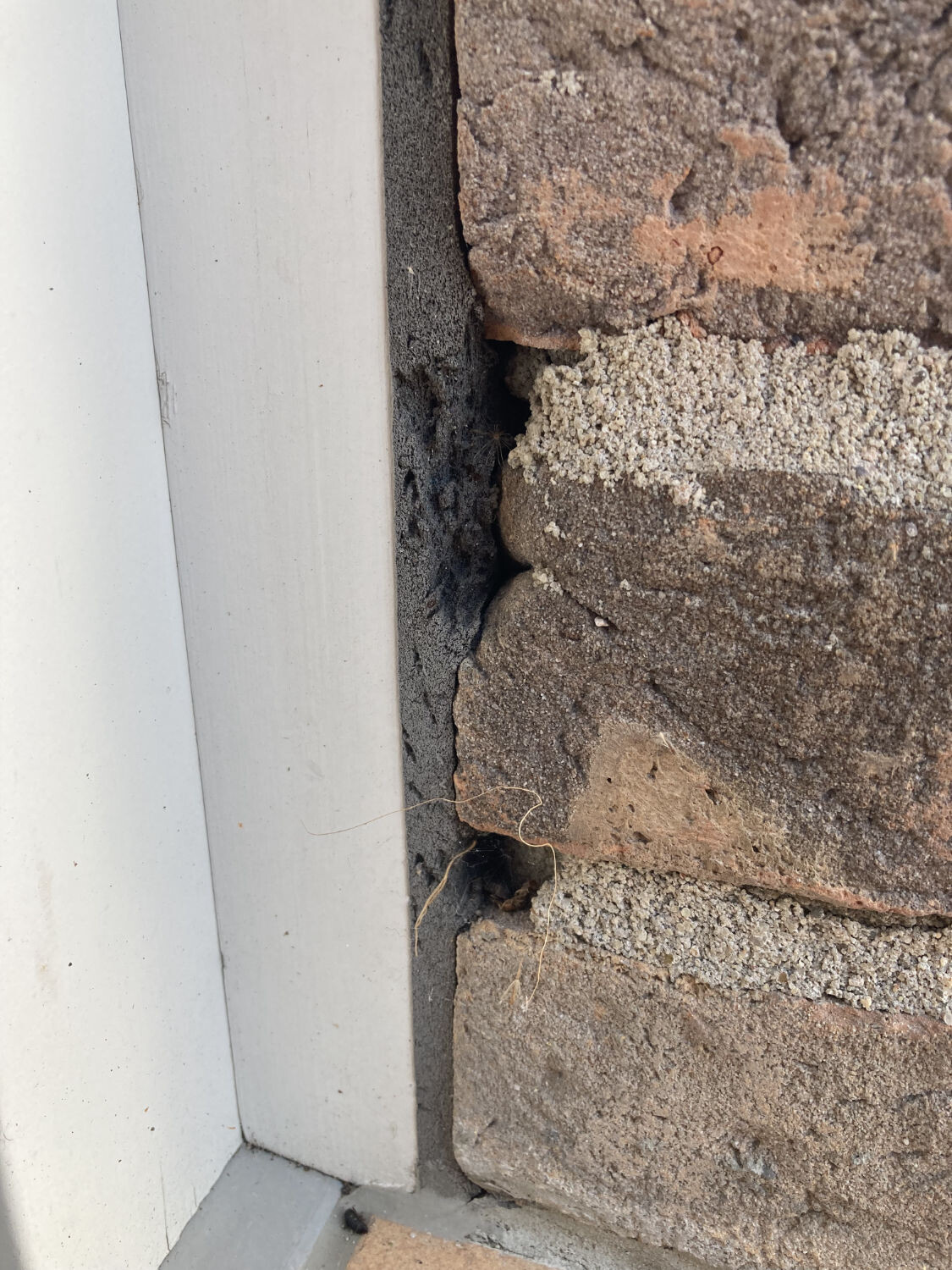 Gap between brick wall and white metal frame; loose, crumbling mortar visible.