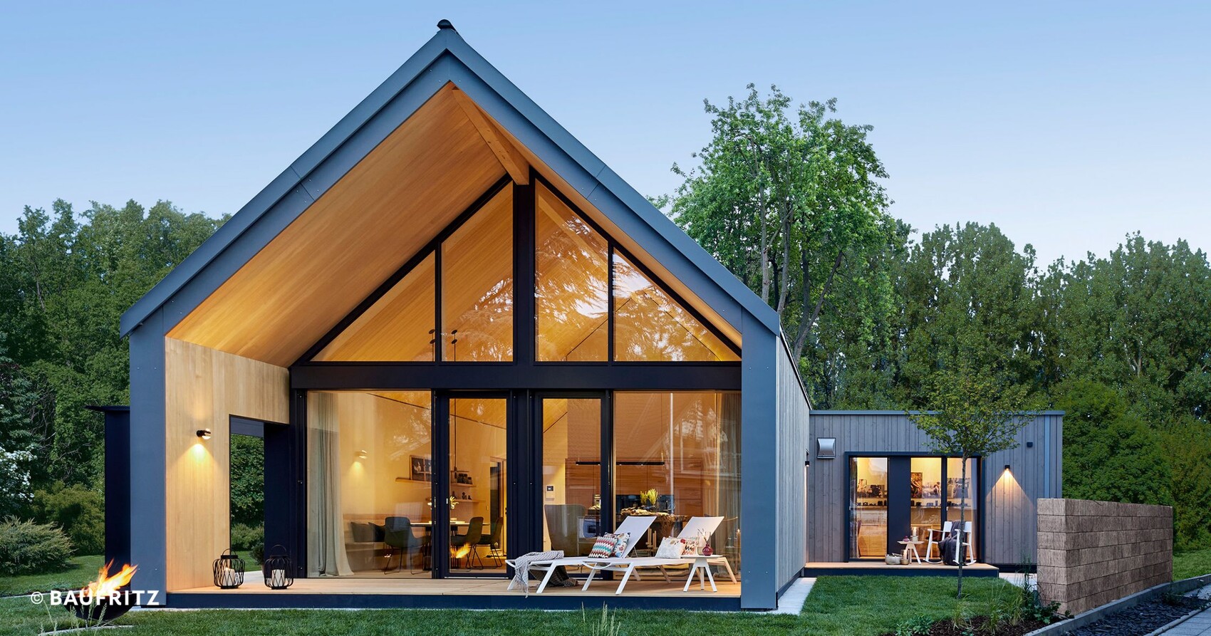 Modern house with large glass facade, warmly lit interior, and garden lounge.