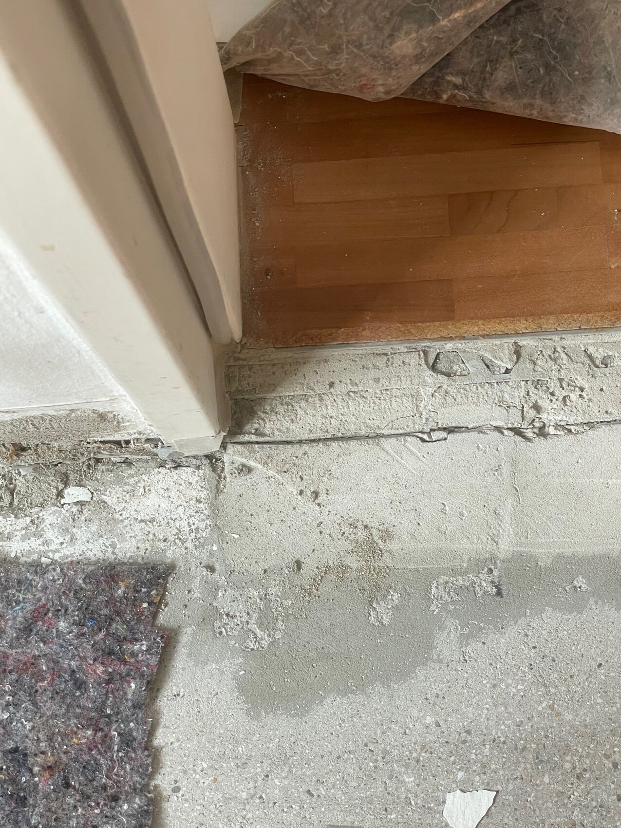 Door threshold: wooden floor behind door, dusty concrete floor and construction debris in front of the transition.