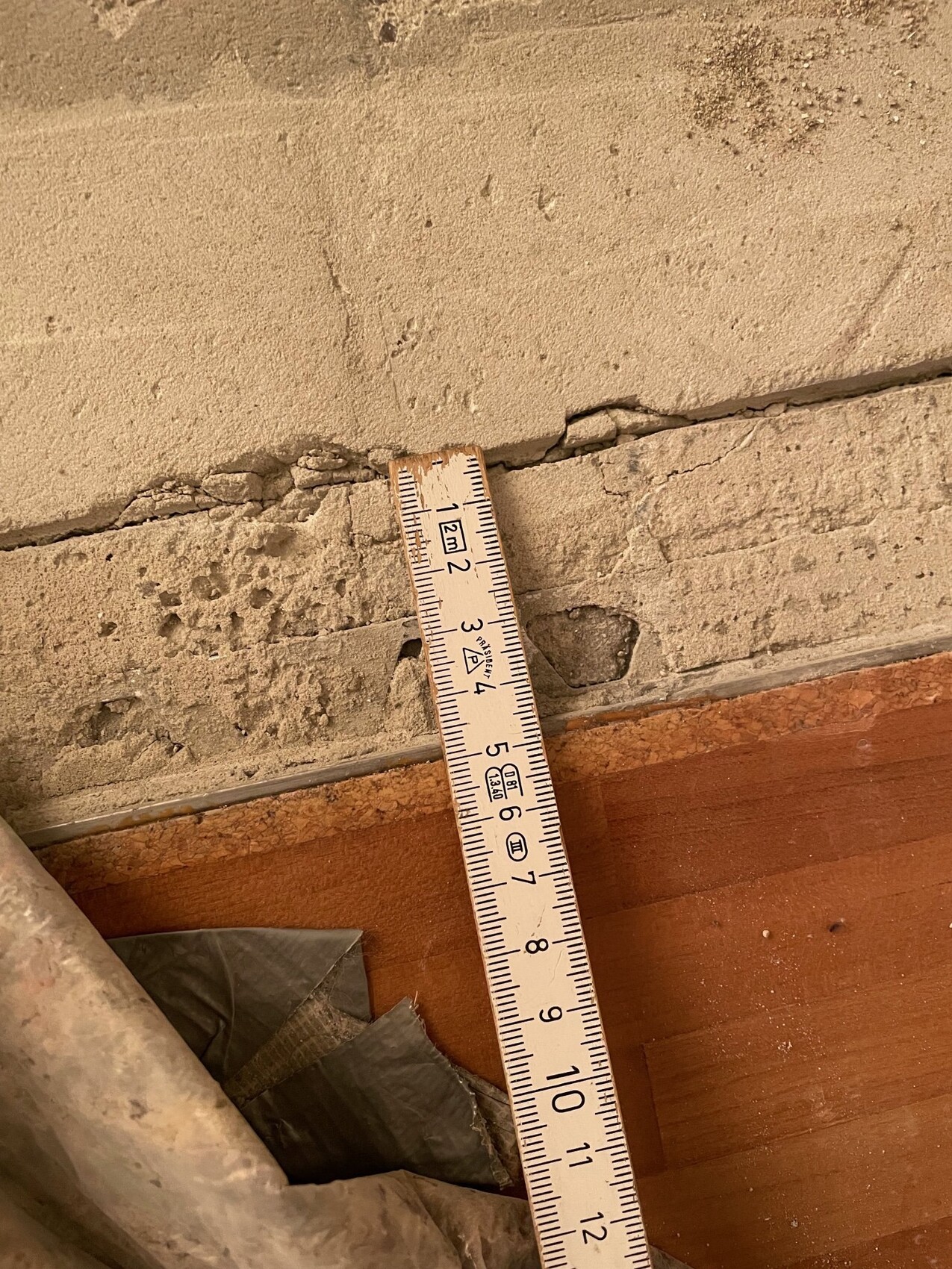 Tape measure resting diagonally on a cracked, plastered wall above a wooden floor.